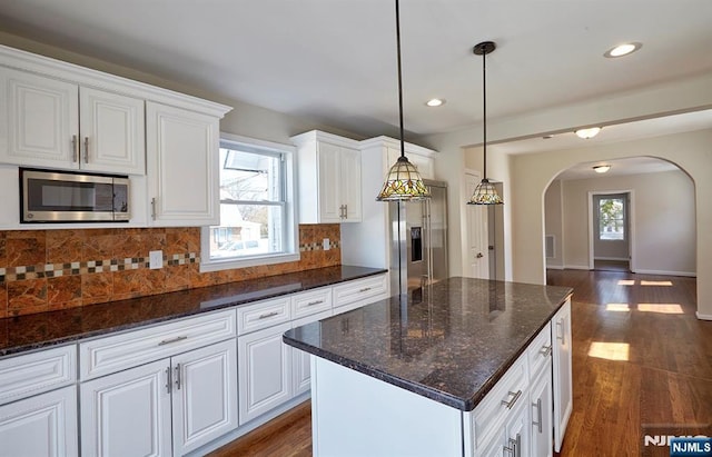 kitchen featuring dark wood-type flooring, white cabinets, arched walkways, and stainless steel appliances