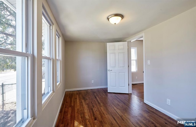 empty room featuring baseboards, dark wood-type flooring, and a healthy amount of sunlight