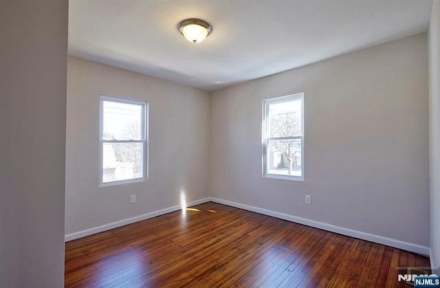 spare room with baseboards, dark wood-type flooring, and a healthy amount of sunlight