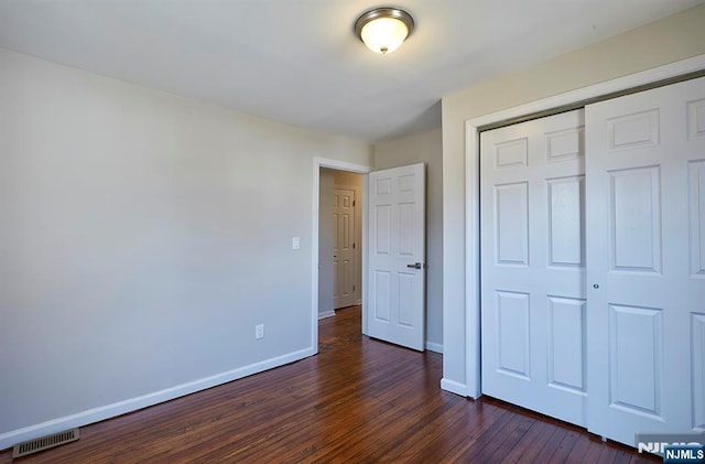 unfurnished bedroom with dark wood-style floors, visible vents, a closet, and baseboards