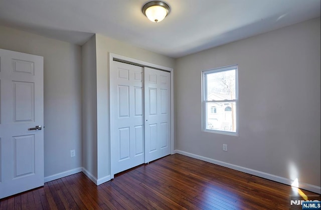 unfurnished bedroom featuring a closet, baseboards, and dark wood-style flooring