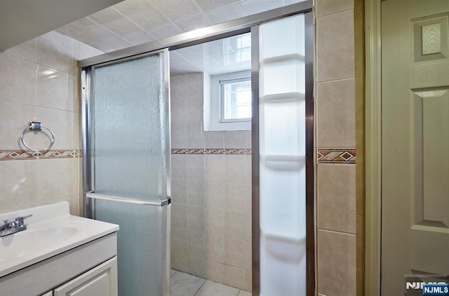 bathroom with marble finish floor, a stall shower, tile walls, and vanity