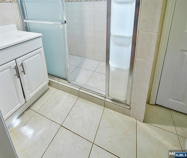 full bathroom featuring tile patterned flooring, a stall shower, tile walls, and vanity