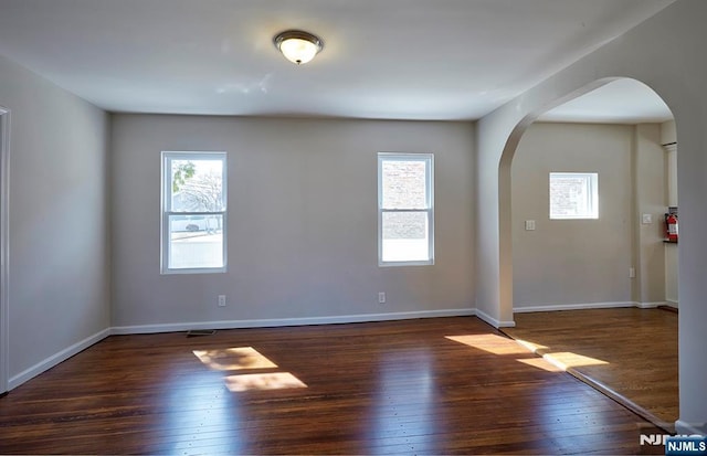 unfurnished room with baseboards, arched walkways, and wood-type flooring