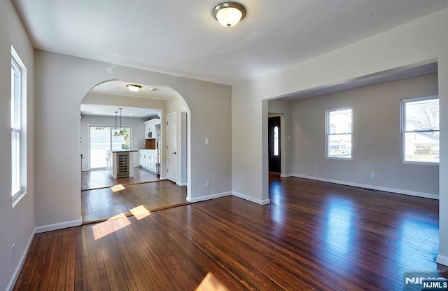 unfurnished room with arched walkways, plenty of natural light, baseboards, and dark wood-style flooring