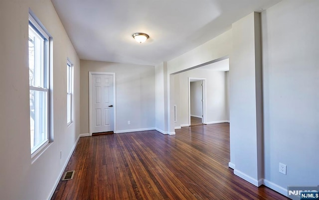 empty room with dark wood-type flooring, baseboards, and visible vents