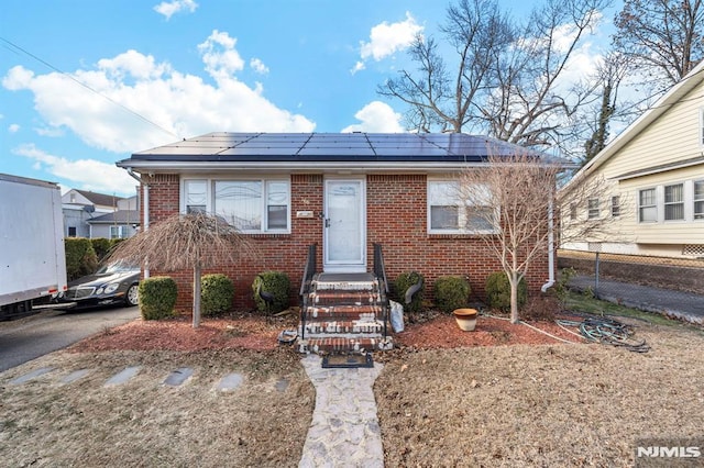 bungalow-style house with brick siding, roof mounted solar panels, and fence