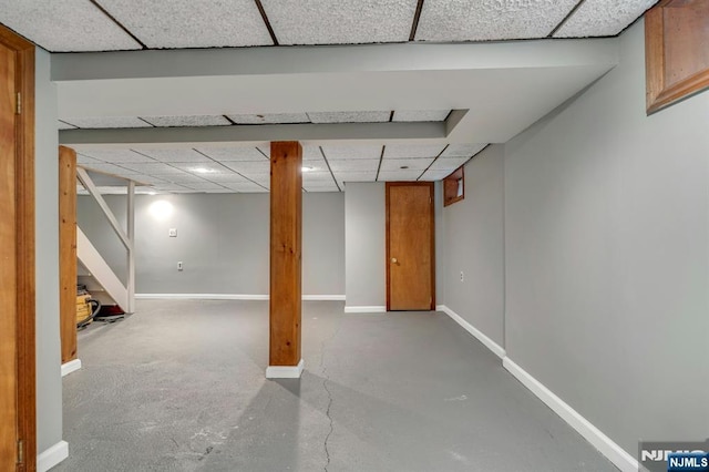 finished below grade area with stairway, a paneled ceiling, and baseboards