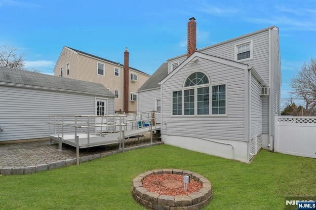 rear view of house with a lawn, a deck, a chimney, and fence