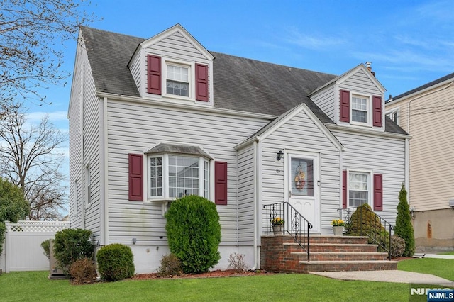 new england style home with a front yard and fence