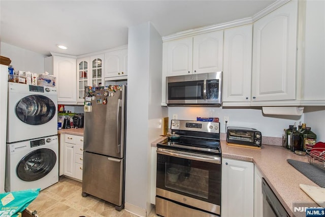 kitchen featuring stacked washer and dryer, white cabinetry, appliances with stainless steel finishes, light countertops, and glass insert cabinets