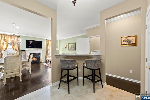 dining area featuring wood finished floors, baseboards, ornamental molding, a lit fireplace, and a chandelier