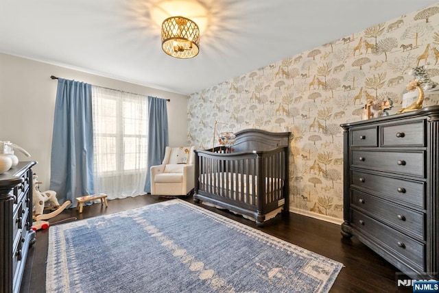 bedroom with baseboards, wallpapered walls, dark wood-style flooring, a crib, and a chandelier