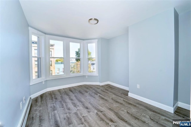 empty room featuring a baseboard heating unit, plenty of natural light, baseboards, and wood finished floors