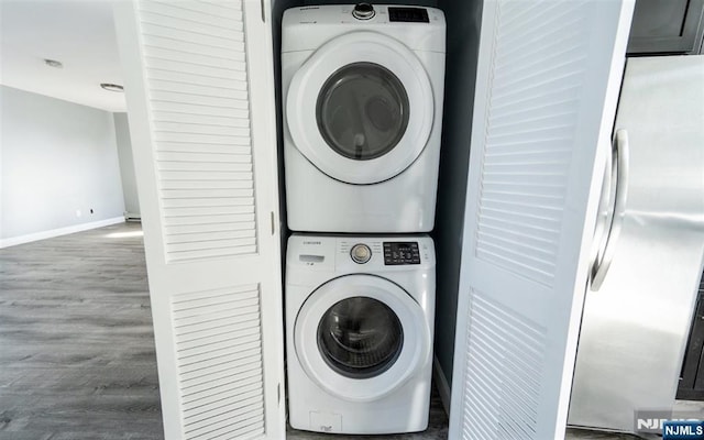 clothes washing area featuring stacked washer / drying machine, baseboards, wood finished floors, and laundry area