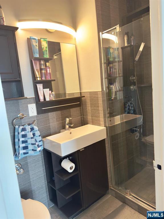 2077 Center Ave Unit 20F, Fort Lee, NJ 07024 - bathroom with vanity, a shower stall, toilet, and tile walls