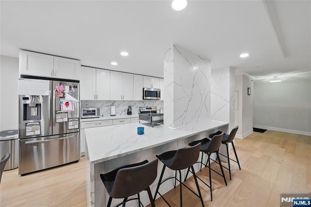 kitchen with a breakfast bar, decorative backsplash, light wood-style flooring, white cabinets, and stainless steel appliances