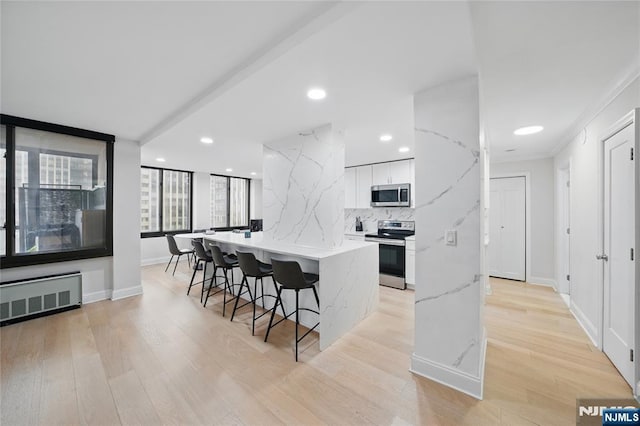 kitchen featuring radiator, a kitchen bar, light wood-style flooring, appliances with stainless steel finishes, and white cabinetry