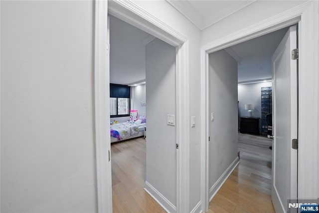 corridor with light wood-style floors, baseboards, and ornamental molding