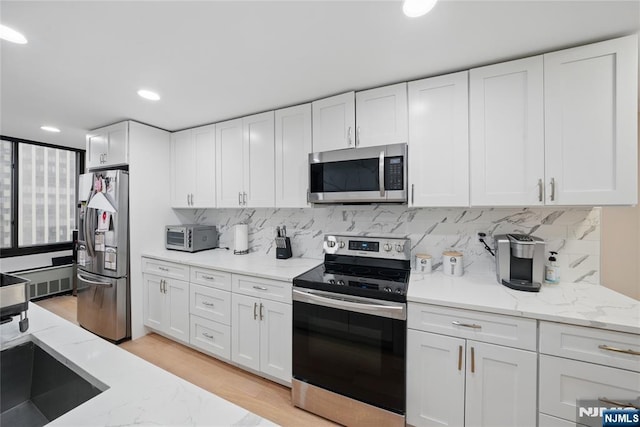 kitchen featuring tasteful backsplash, white cabinetry, stainless steel appliances, light wood-style floors, and light stone countertops