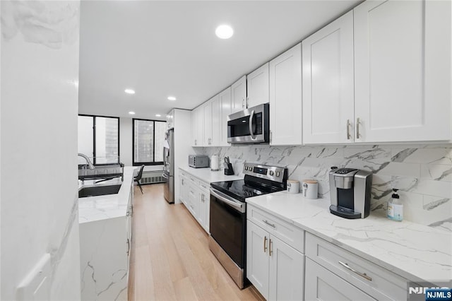 kitchen featuring a sink, white cabinetry, stainless steel appliances, light wood-style floors, and decorative backsplash