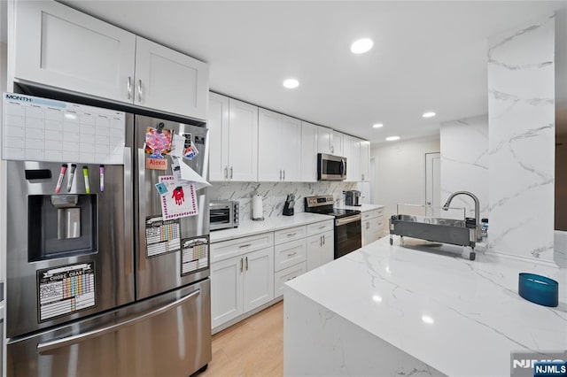 kitchen with light wood-style flooring, stainless steel appliances, white cabinets, decorative backsplash, and light stone countertops