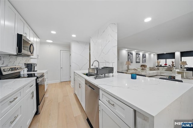 kitchen featuring light wood finished floors, a sink, decorative backsplash, stainless steel appliances, and white cabinets