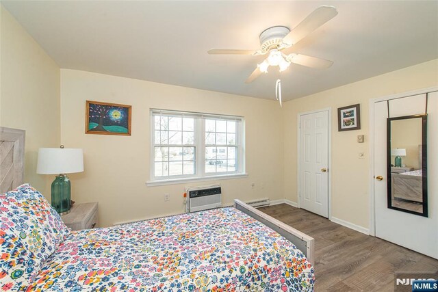 bedroom featuring a ceiling fan, a wall mounted AC, wood finished floors, a baseboard radiator, and baseboards