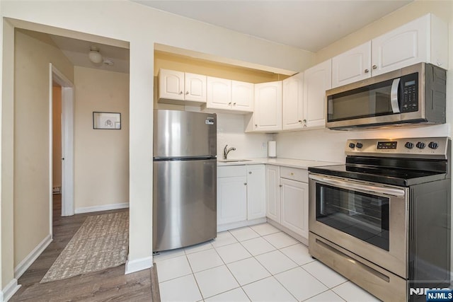 kitchen featuring a sink, appliances with stainless steel finishes, white cabinets, light countertops, and baseboards