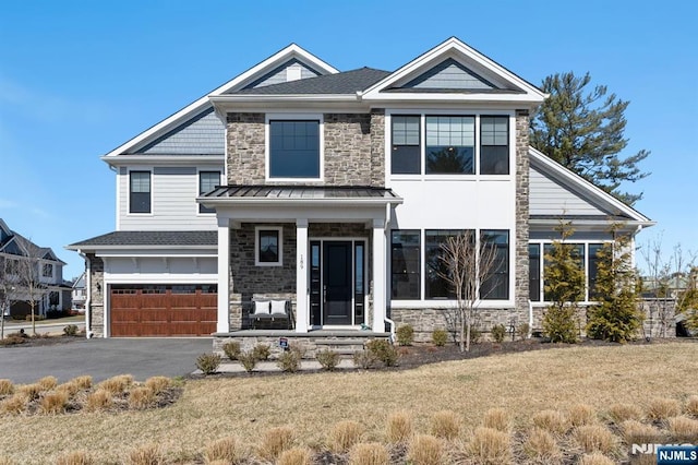 view of front of home featuring stone siding, aphalt driveway, a garage, a front lawn, and a porch