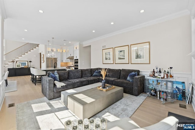 living room featuring stairs, ornamental molding, a wainscoted wall, visible vents, and light wood-style flooring