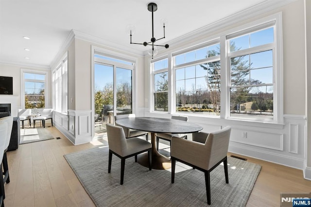 dining room featuring crown molding, light wood-style flooring, a decorative wall, and a healthy amount of sunlight