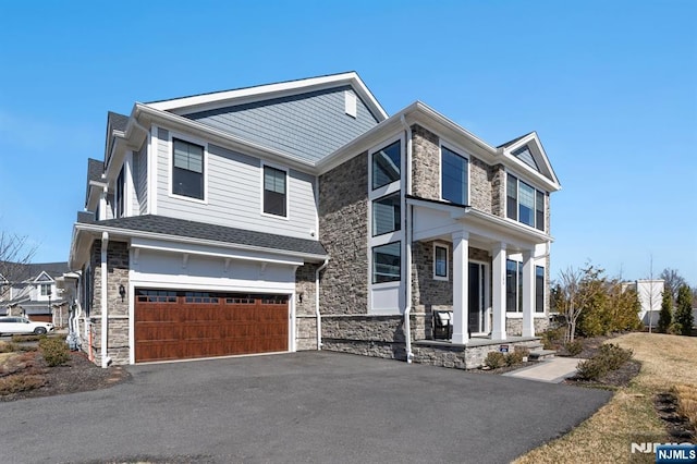 view of front of house with a porch, an attached garage, stone siding, and aphalt driveway