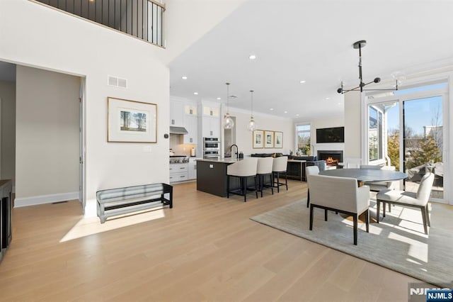 dining room featuring light wood-style flooring, visible vents, ornamental molding, recessed lighting, and a lit fireplace