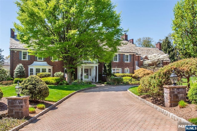 view of front of home with brick siding, a high end roof, and a chimney
