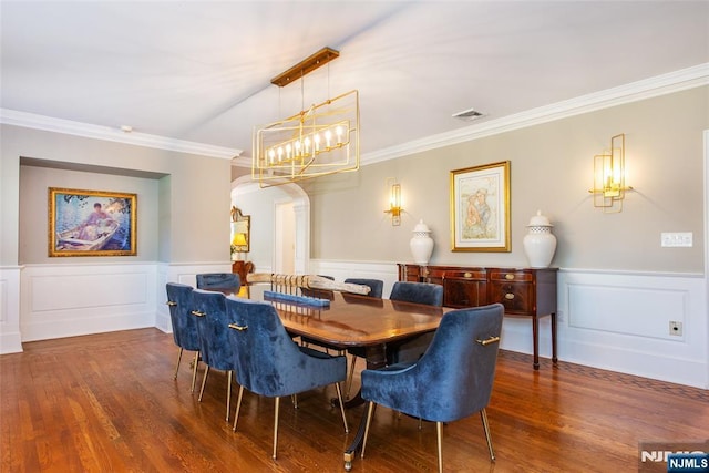 dining room featuring visible vents, arched walkways, wood finished floors, an inviting chandelier, and ornamental molding
