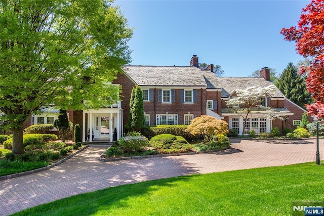 shingle-style home featuring a high end roof, a chimney, a front lawn, and brick siding