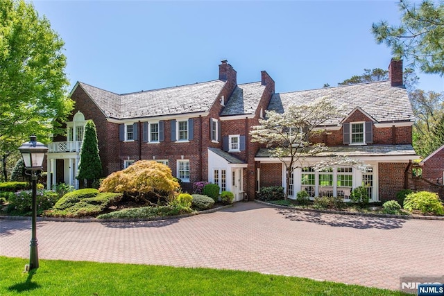 view of front of property with brick siding, a high end roof, and a chimney