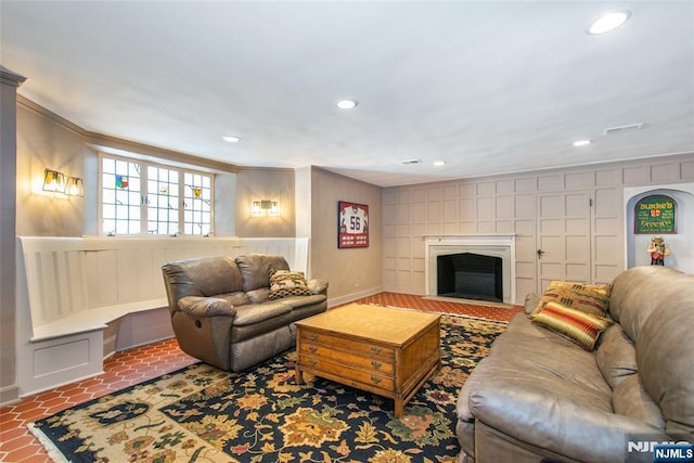 living room featuring crown molding, a fireplace, a decorative wall, and recessed lighting