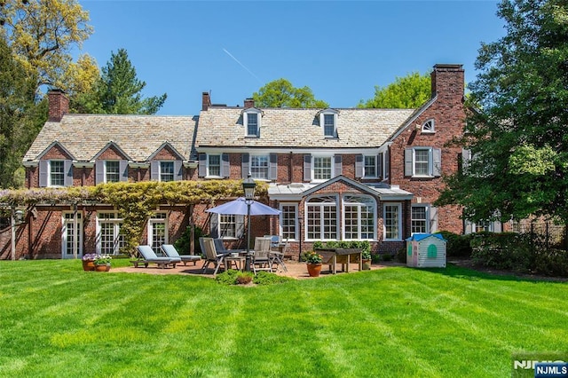 back of house featuring a high end roof, a chimney, a yard, and a patio