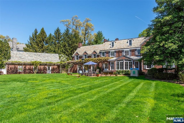 rear view of house with a yard, a high end roof, a chimney, and a patio area