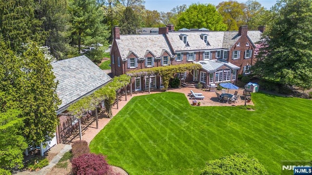 rear view of property with a high end roof, a chimney, french doors, a lawn, and a patio area