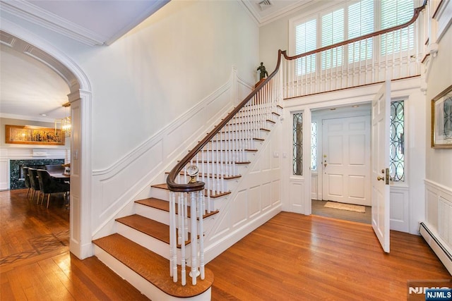 foyer featuring a baseboard heating unit, ornamental molding, wood finished floors, and a decorative wall