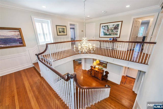 stairway with an inviting chandelier, a decorative wall, wood finished floors, and a healthy amount of sunlight