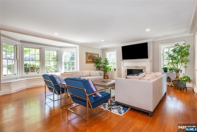 living room with crown molding, a high end fireplace, light wood finished floors, and a healthy amount of sunlight