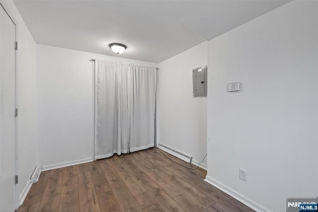 empty room featuring electric panel, a baseboard heating unit, baseboards, and wood finished floors