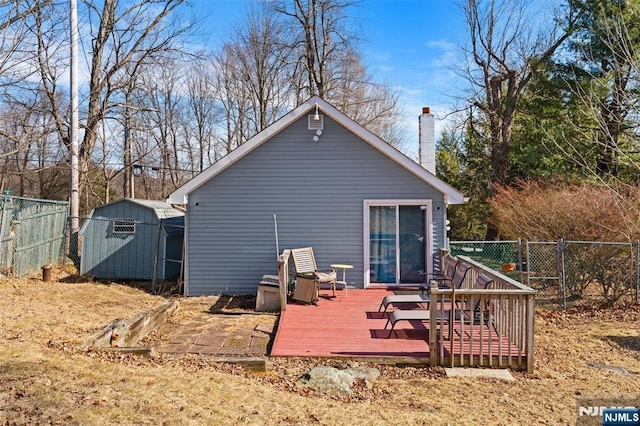 back of property with an outbuilding, a fenced backyard, a storage shed, a wooden deck, and a chimney