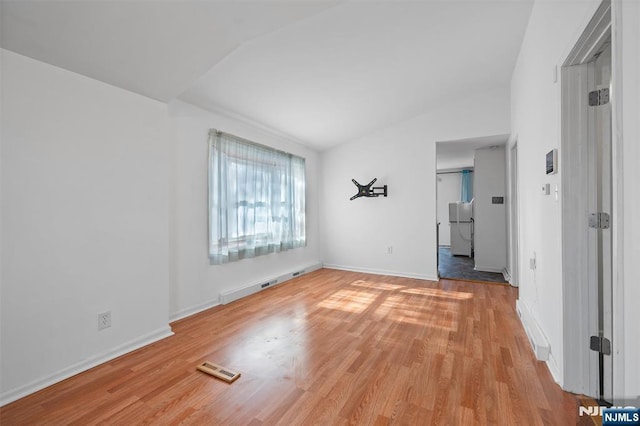 empty room featuring lofted ceiling, light wood-style floors, baseboards, and visible vents