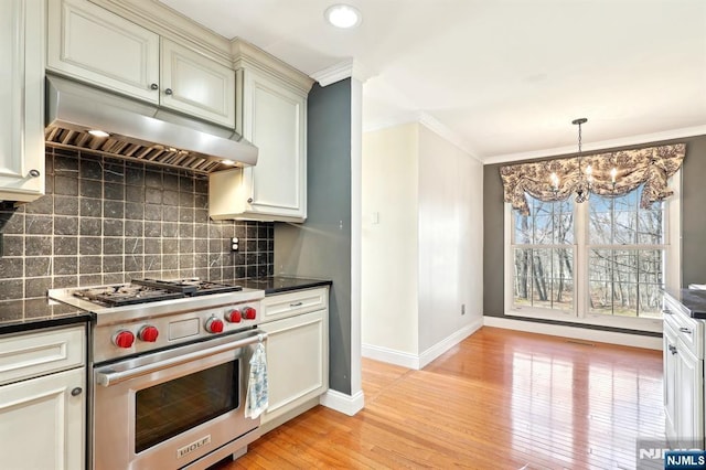 kitchen featuring premium range, ornamental molding, dark countertops, under cabinet range hood, and an inviting chandelier