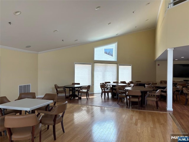 dining room with visible vents, a towering ceiling, crown molding, and light wood-type flooring